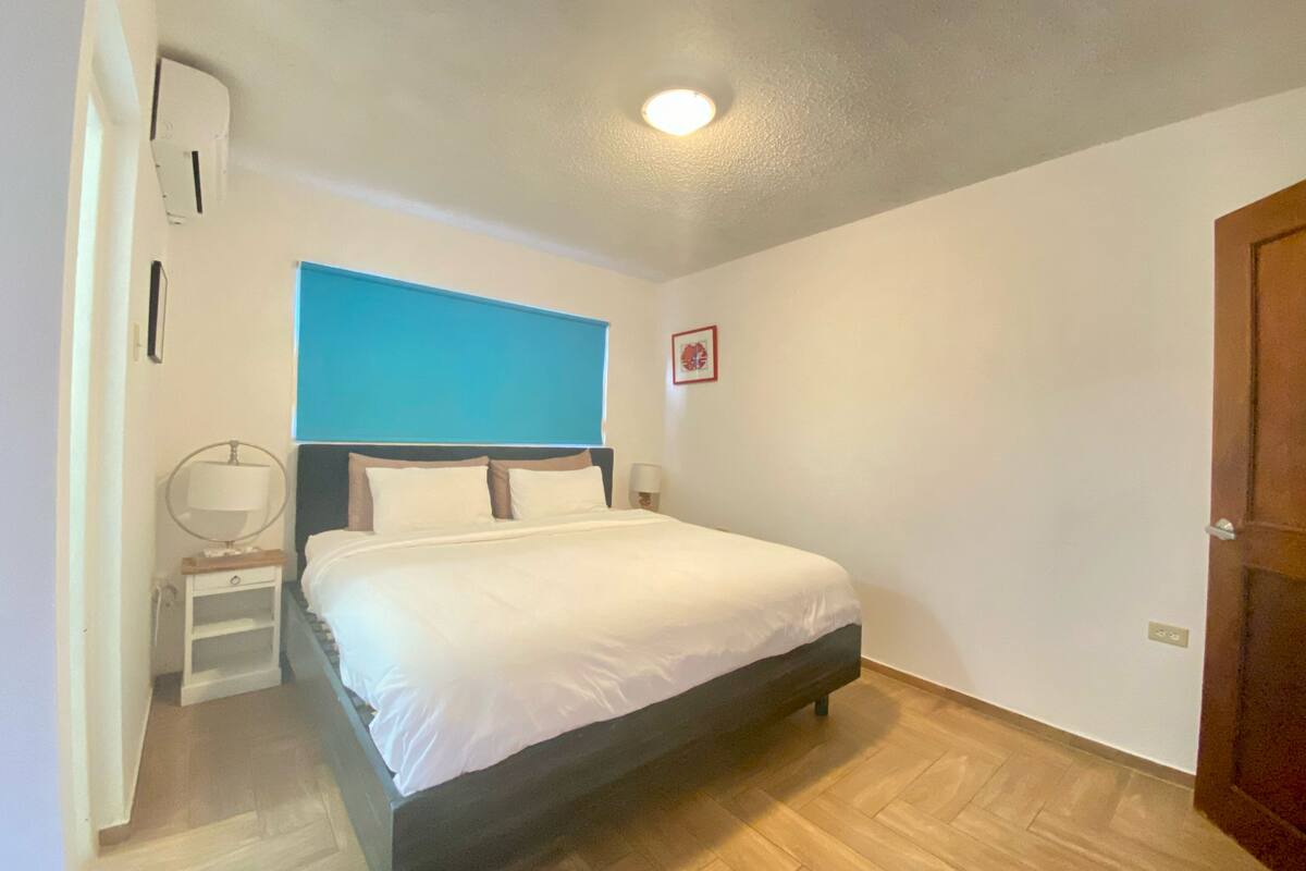 Une chambre à coucher comprenant un lit, des tables de chevet, un climatiseur fixé au mur et une porte.