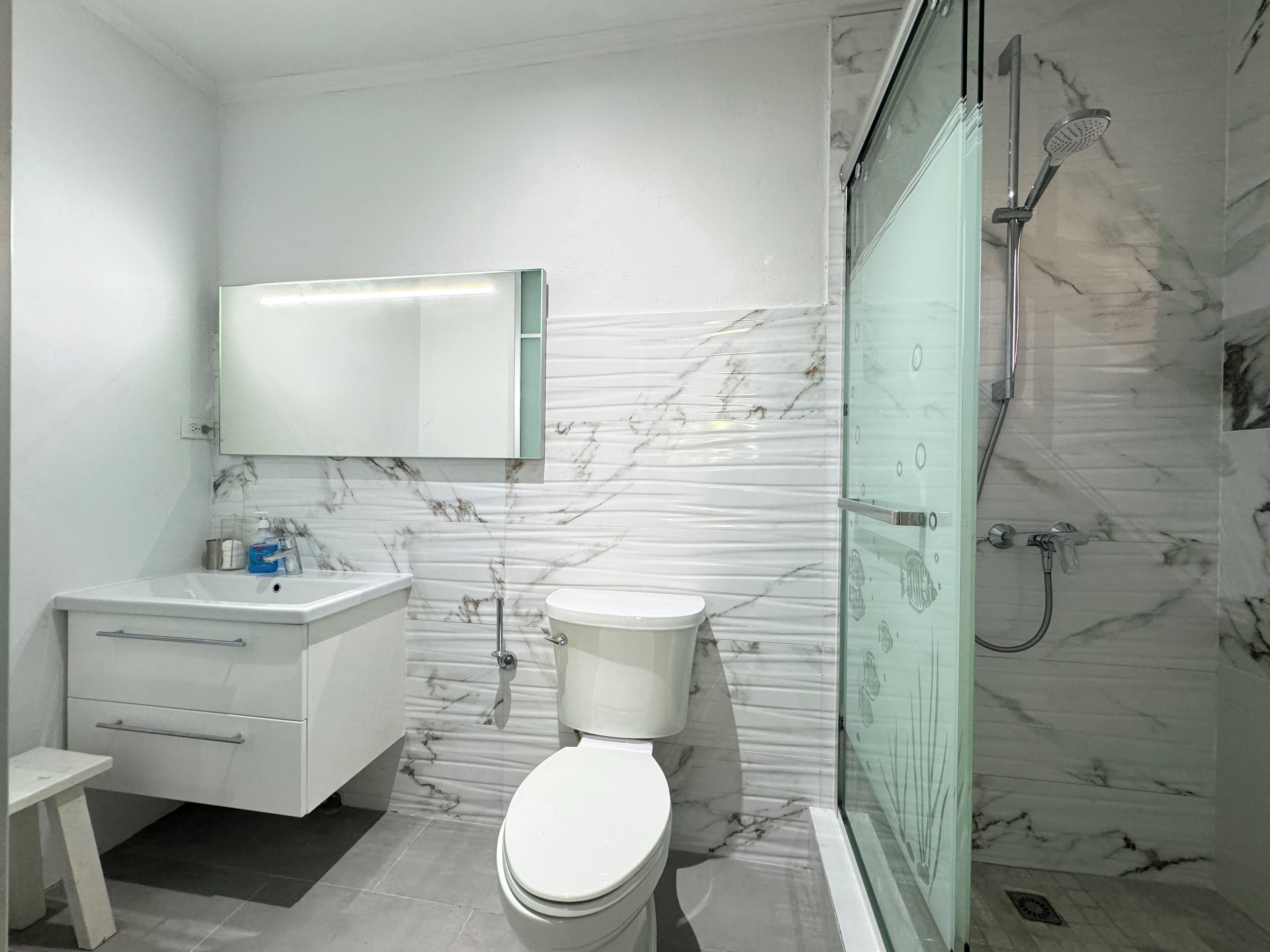 A modern bathroom with a toilet, vanity, and a glass-enclosed shower.