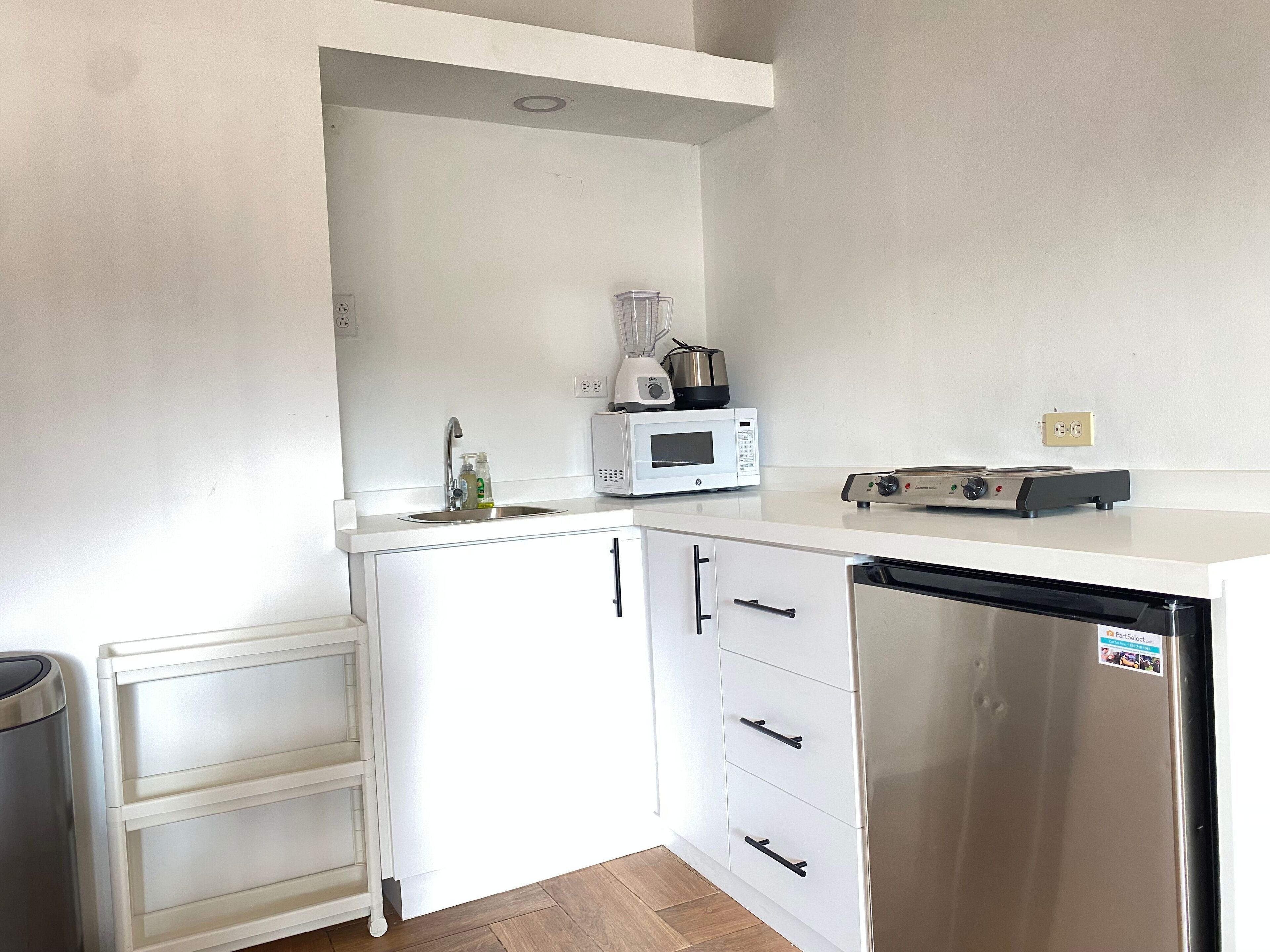 Una cocina compacta con armarios blancos, un refrigerador de acero inoxidable, un microondas y un tostador.