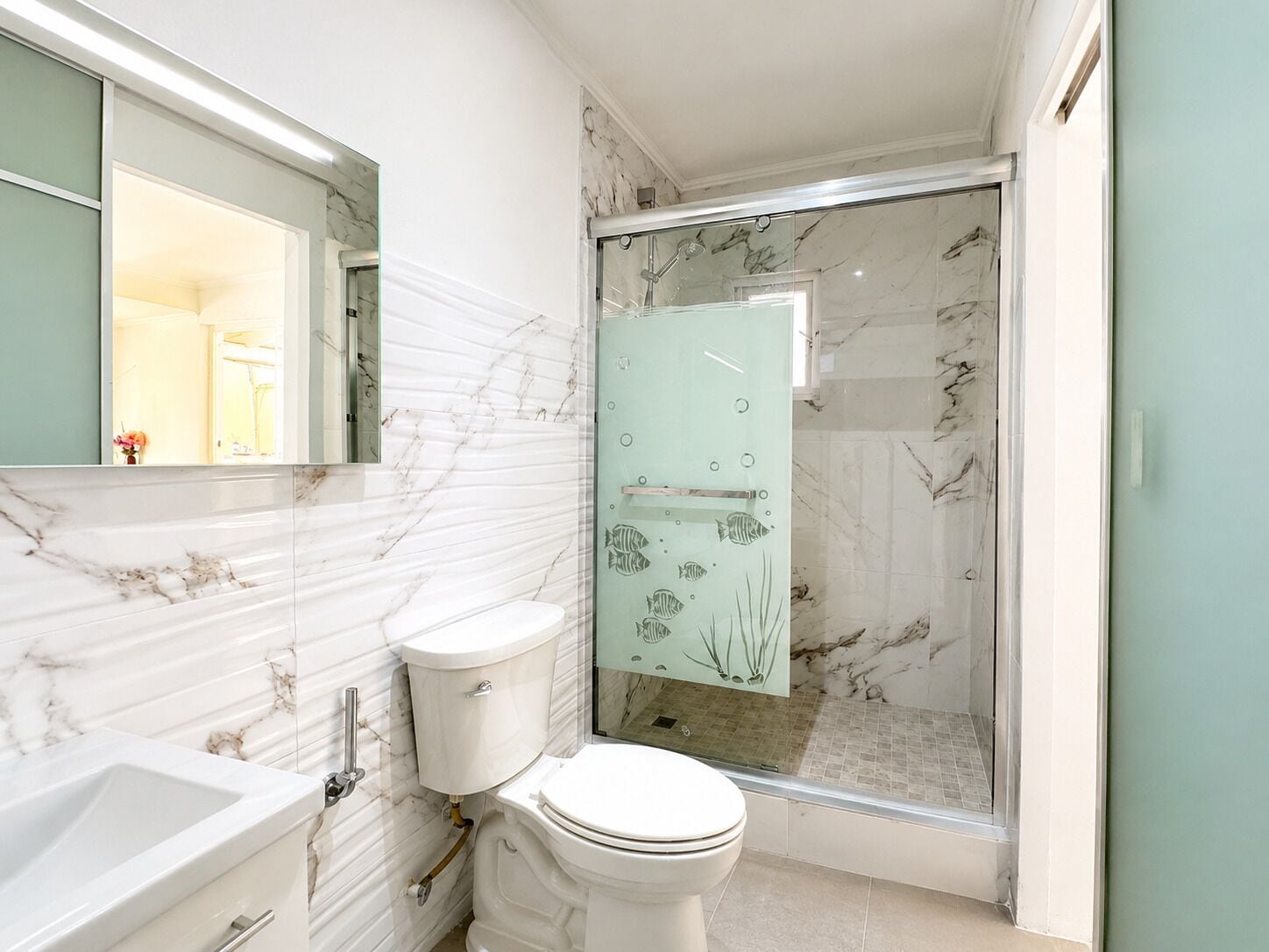 Un baño con tocador de mármol, inodoro y ducha con mampara de vidrio.