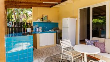 A compact kitchen with a blue tiled backsplash, a white refrigerator, and a small dining area with a white table and metal chairs.