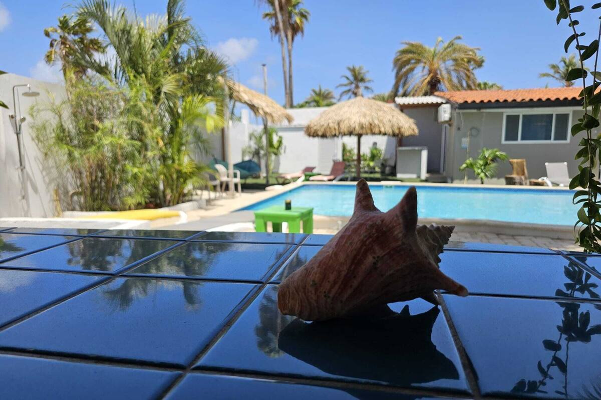 Un espace piscine avec une eau d’un bleu limpide, des chaises longues et un parasol en chaume.