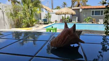 Zona de piscina con una piscina azul cristalina, sillas de descanso y una sombrilla de paja.
