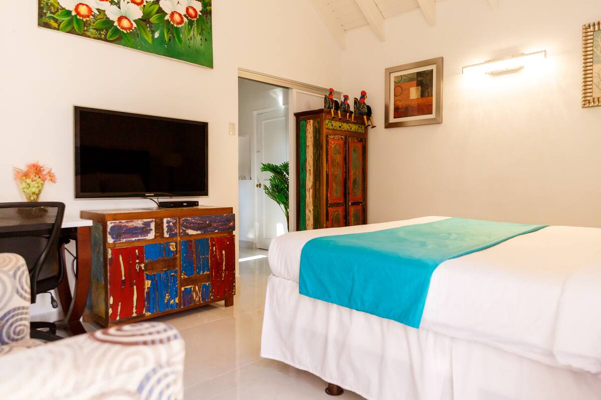 Une chambre d’hôtel avec un lit, une télévision, une armoire aux couleurs vives et une porte donnant sur une autre pièce.