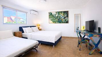 A bedroom with two beds, a desk with a TV, and a large window.