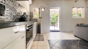 A kitchen with patterned tiles, a built-in oven, a sink, and a window overlooking a garden. - Casalina Garden Apartment Aruba (Noord)