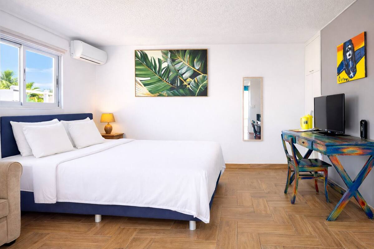 Une chambre à coucher comprenant un lit, un bureau, une chaise, une lampe et des œuvres d’art accrochées aux murs.