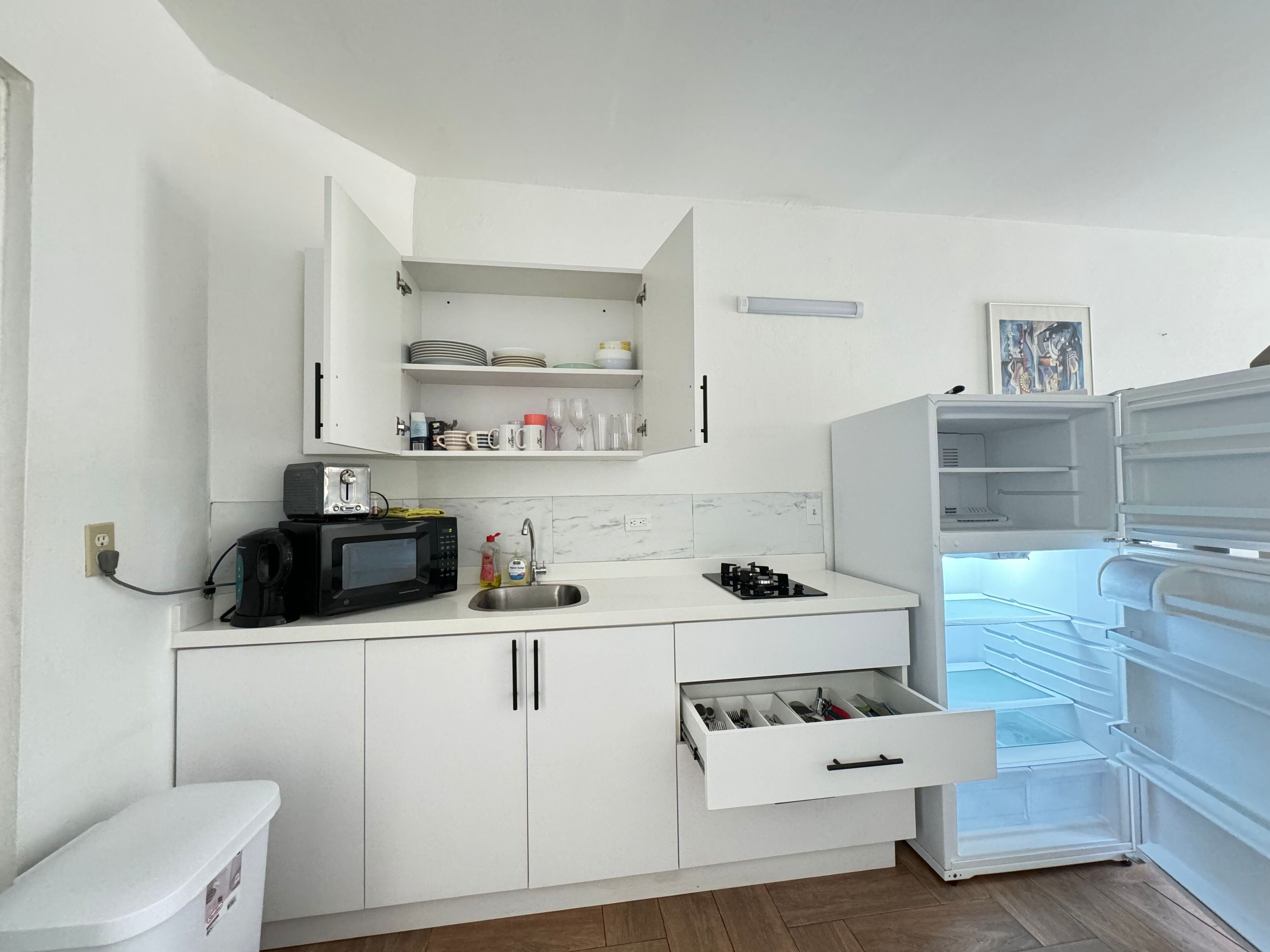 Eine kleine Küche mit weißen Schränken, einer Mikrowelle, einem Toaster, einem Spülbecken und einem Kühlschrank.