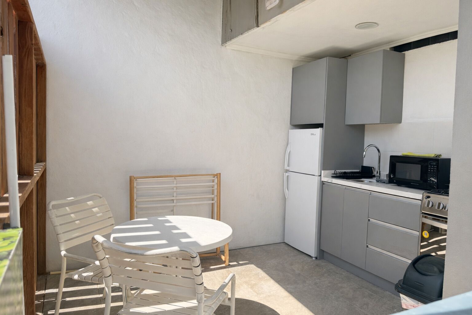 Cocina compacta con refrigerador, microondas y horno. Se incluye una pequeña mesa de comedor con sillas.