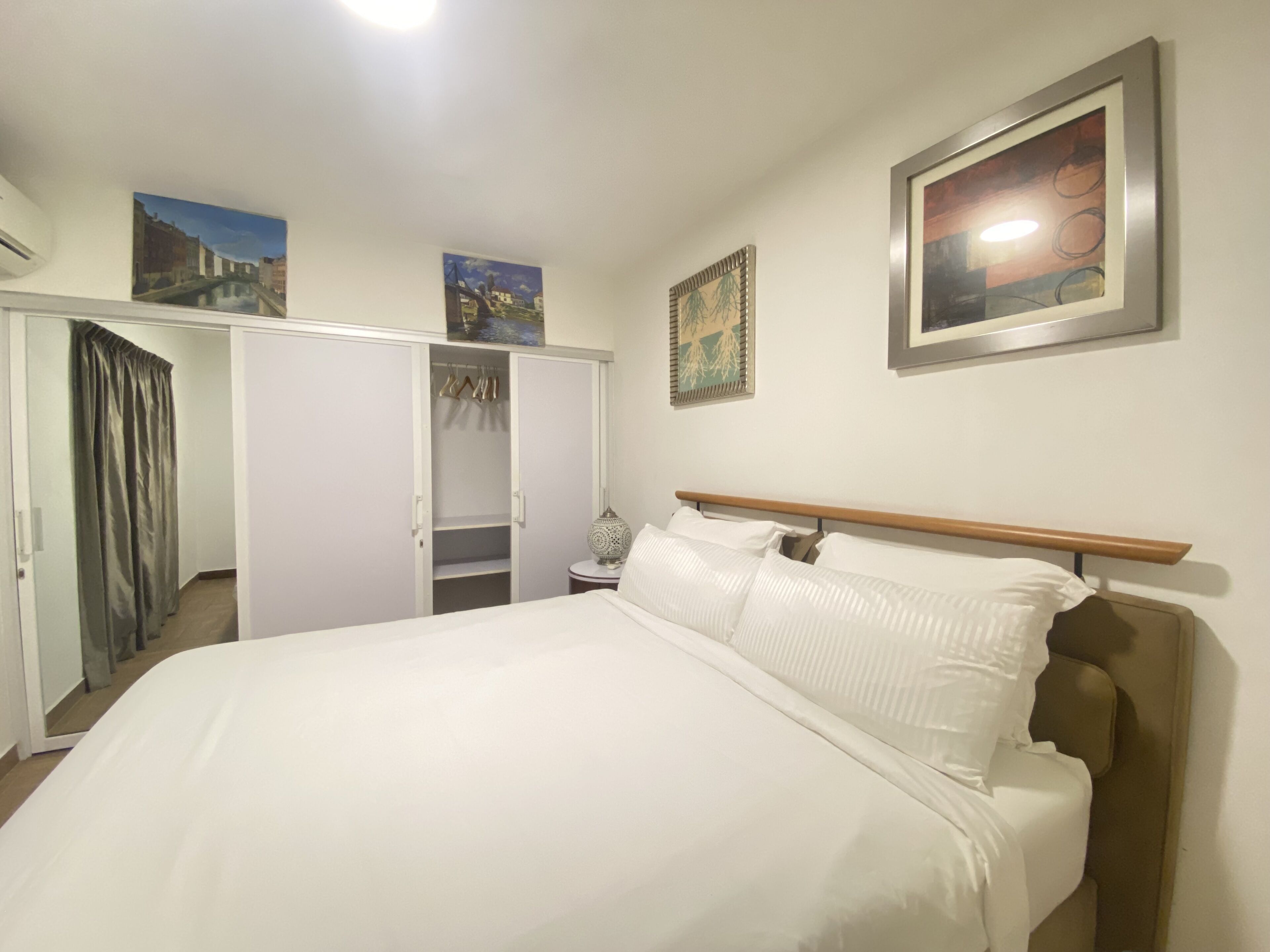 A bedroom with a large bed, a wardrobe, and two wall-mounted paintings.