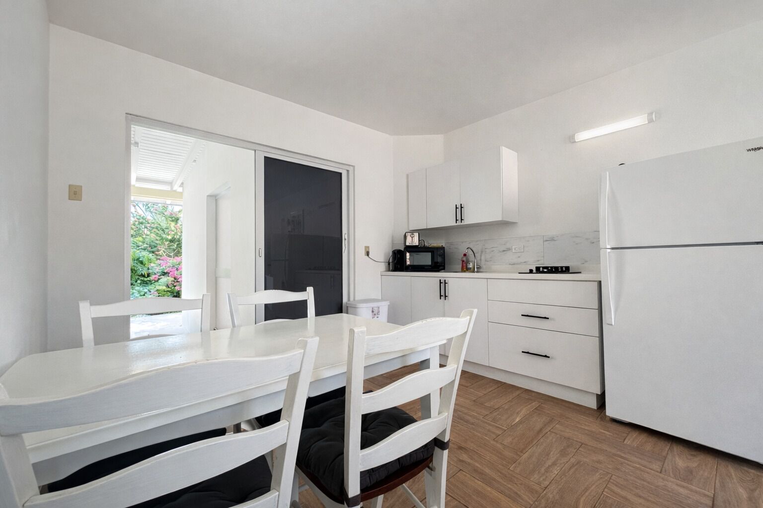 Eine kleine Küche mit weißen Schränken, einem Esstisch mit Stühlen, einem Kühlschrank und einer Mikrowelle.