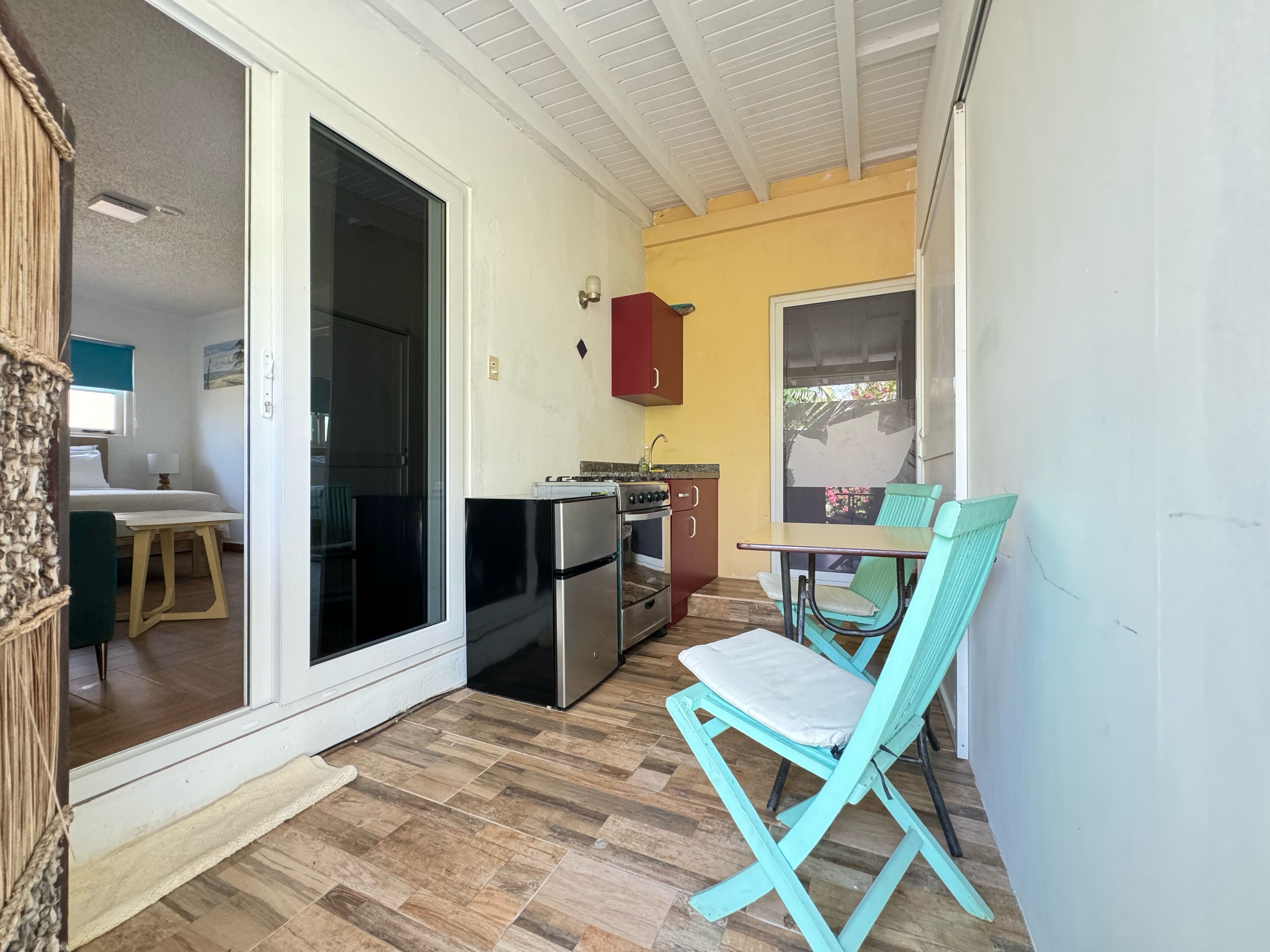 A small kitchen with a refrigerator, stove, and sink. There is a dining table with a chair.