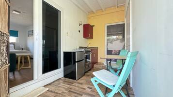 A small kitchen with a refrigerator, stove, and sink. There is a dining table with a chair.