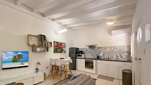 A living room with a sofa, TV, and dining area with chairs and a table. - Casalina Garden Apartment Aruba (Noord)