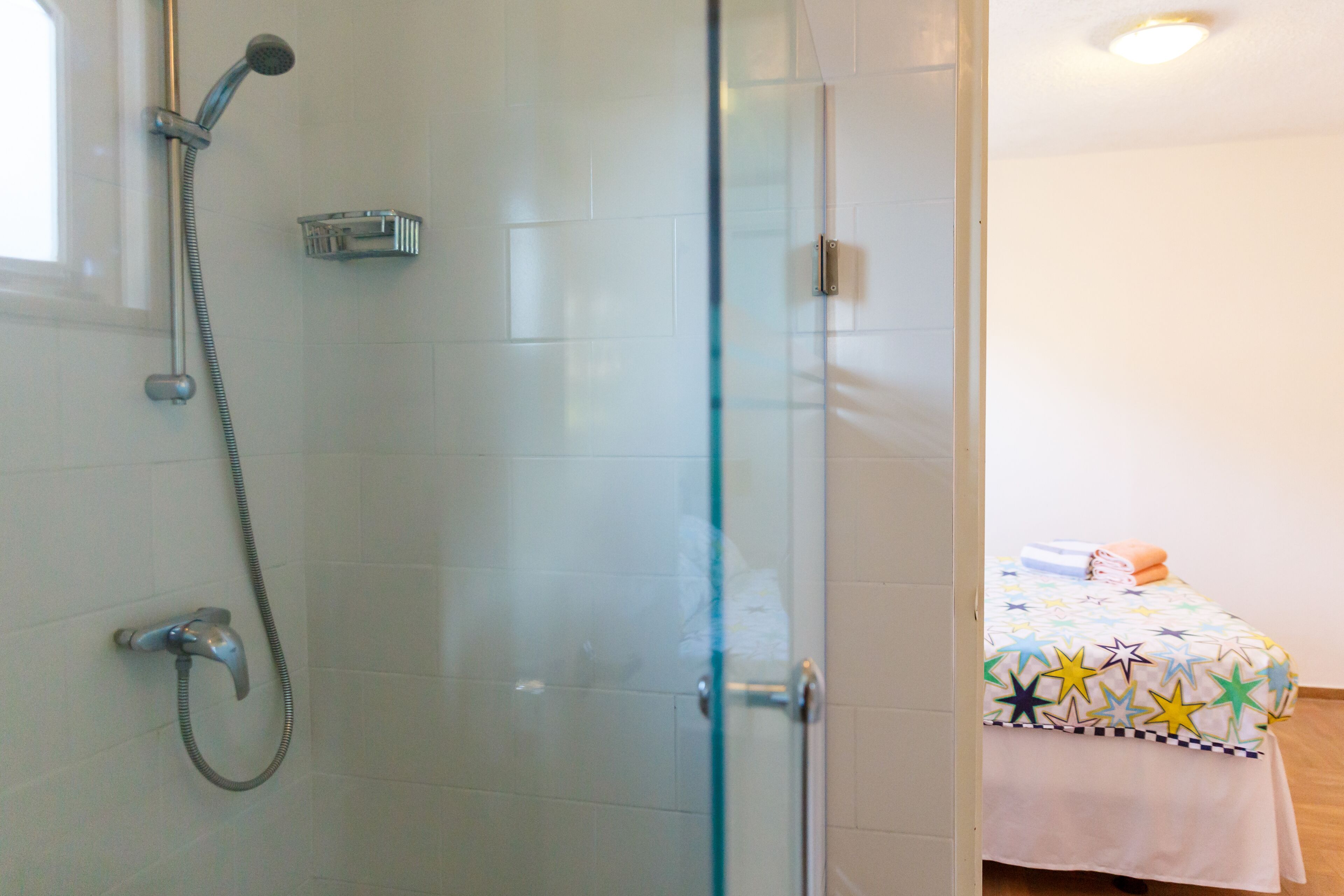Een badkamer met een glazen douchecabine, een handdouche en een wandmengkraan.