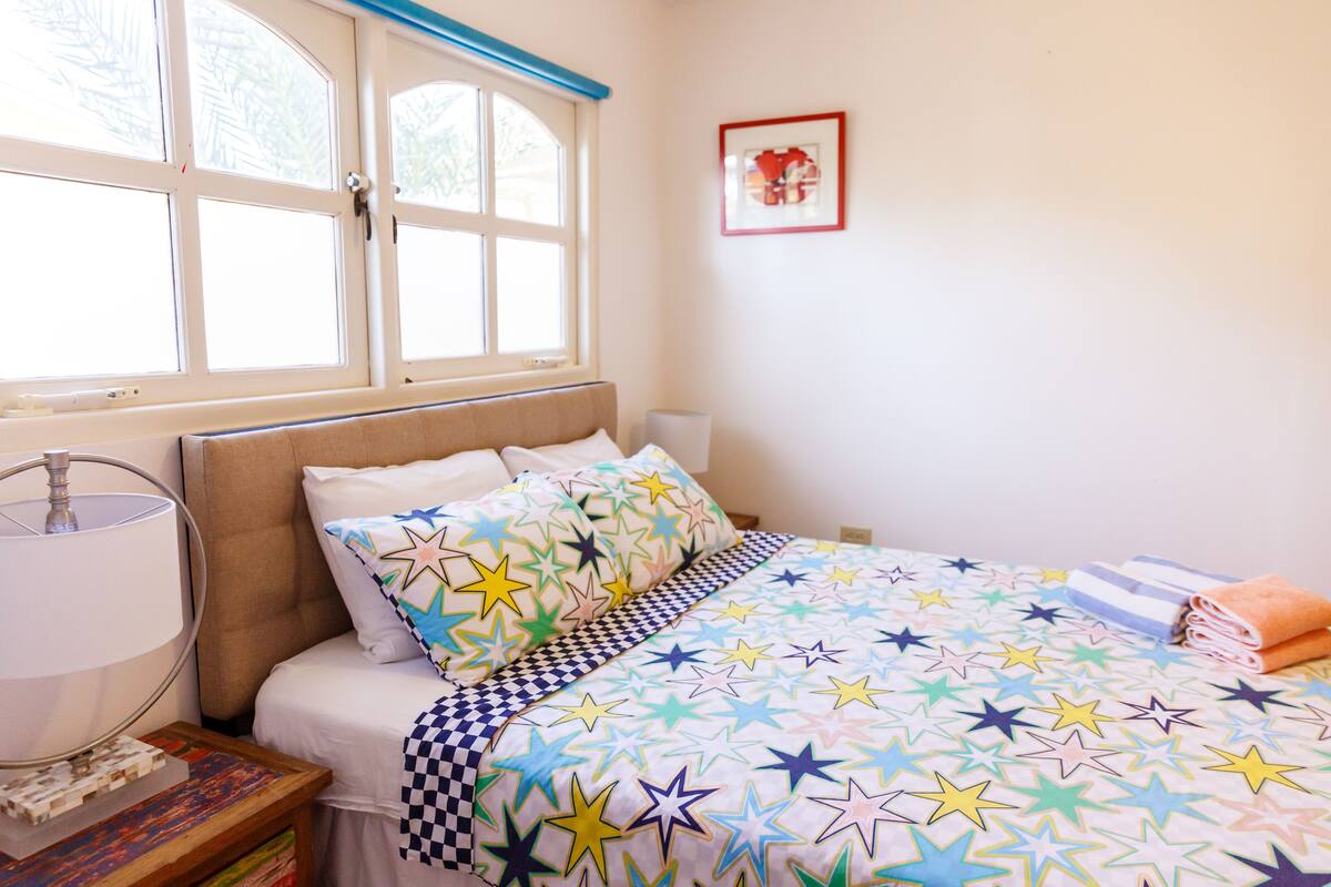 Une chambre à coucher avec un lit, une lampe de chevet, une fenêtre et un tableau encadré au mur.