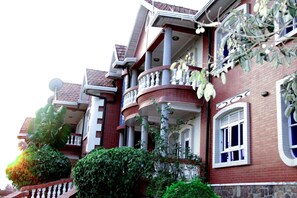 A multi-story building with a brick facade, balconies with white railings, and a mix of windows and doors.
