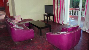 A living room with two purple sofas, a black coffee table, and a television on a stand. - Diplomat Apartment Kacyiru (Kigali)