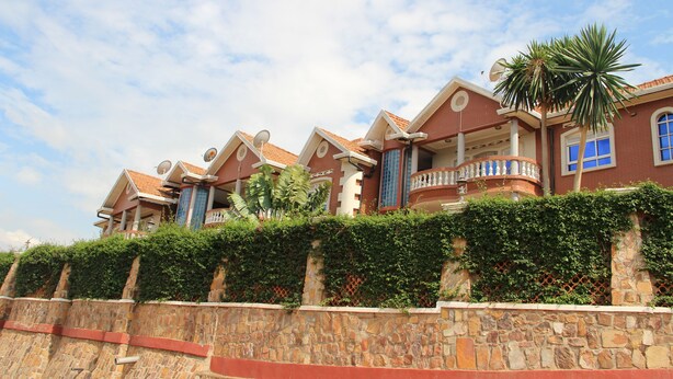 A multi-story building with a stone facade, balconies, and a lush green hedge. - Diplomat Apartment Kacyiru (Kigali)