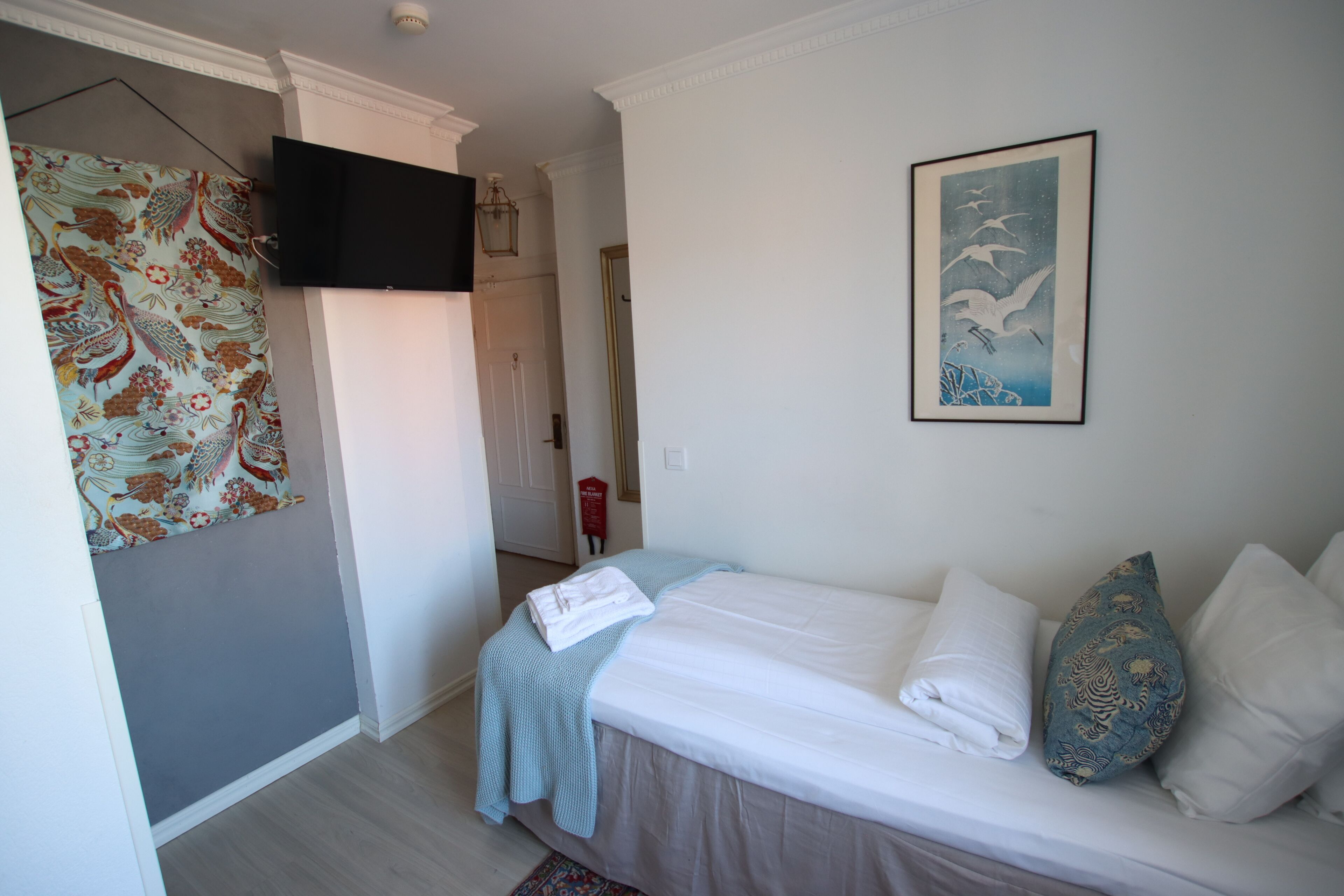 Een slaapkamer met een bed, kussens, een flatscreen televisie, een ingelijste afbeelding en een kamerbreed gordijn.
