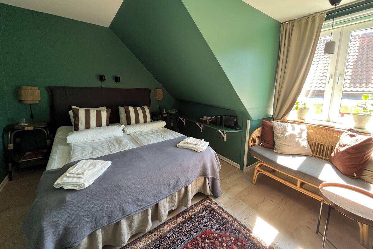 A bedroom with a bed, bedside tables, a chair, a window with curtains, and a view of the outside.