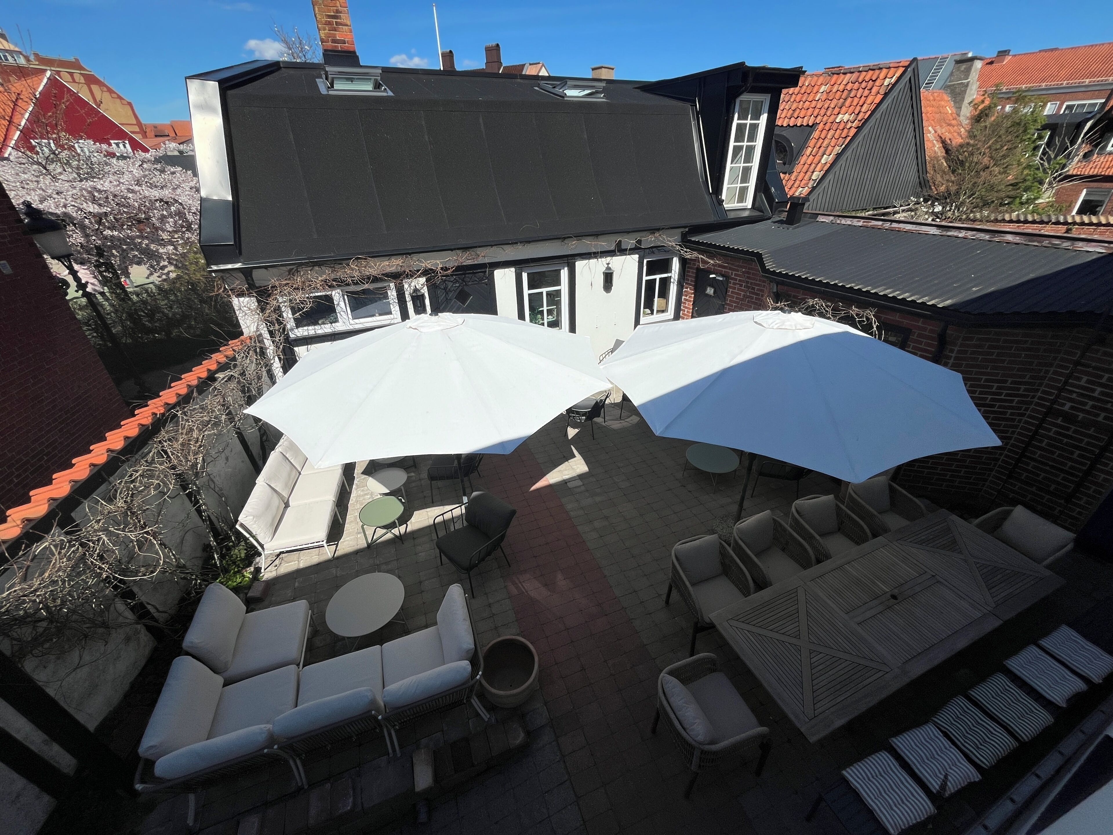 A rooftop patio with outdoor seating, including lounge chairs and tables, and large umbrellas providing shade.