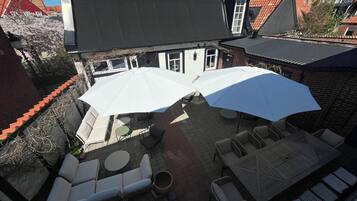 A rooftop patio with outdoor seating, including lounge chairs and tables, and large umbrellas providing shade.