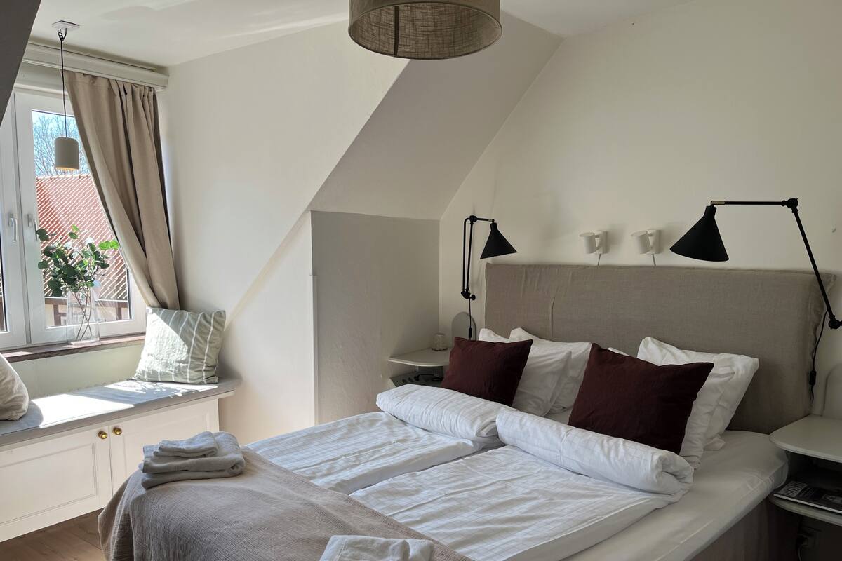 A bedroom with a bed, bedside tables, a window with curtains, and a lamp.
