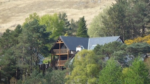 A two-story house with a balcony, surrounded by dense trees and a hill in the background. - Treetops B&B (Fort William)