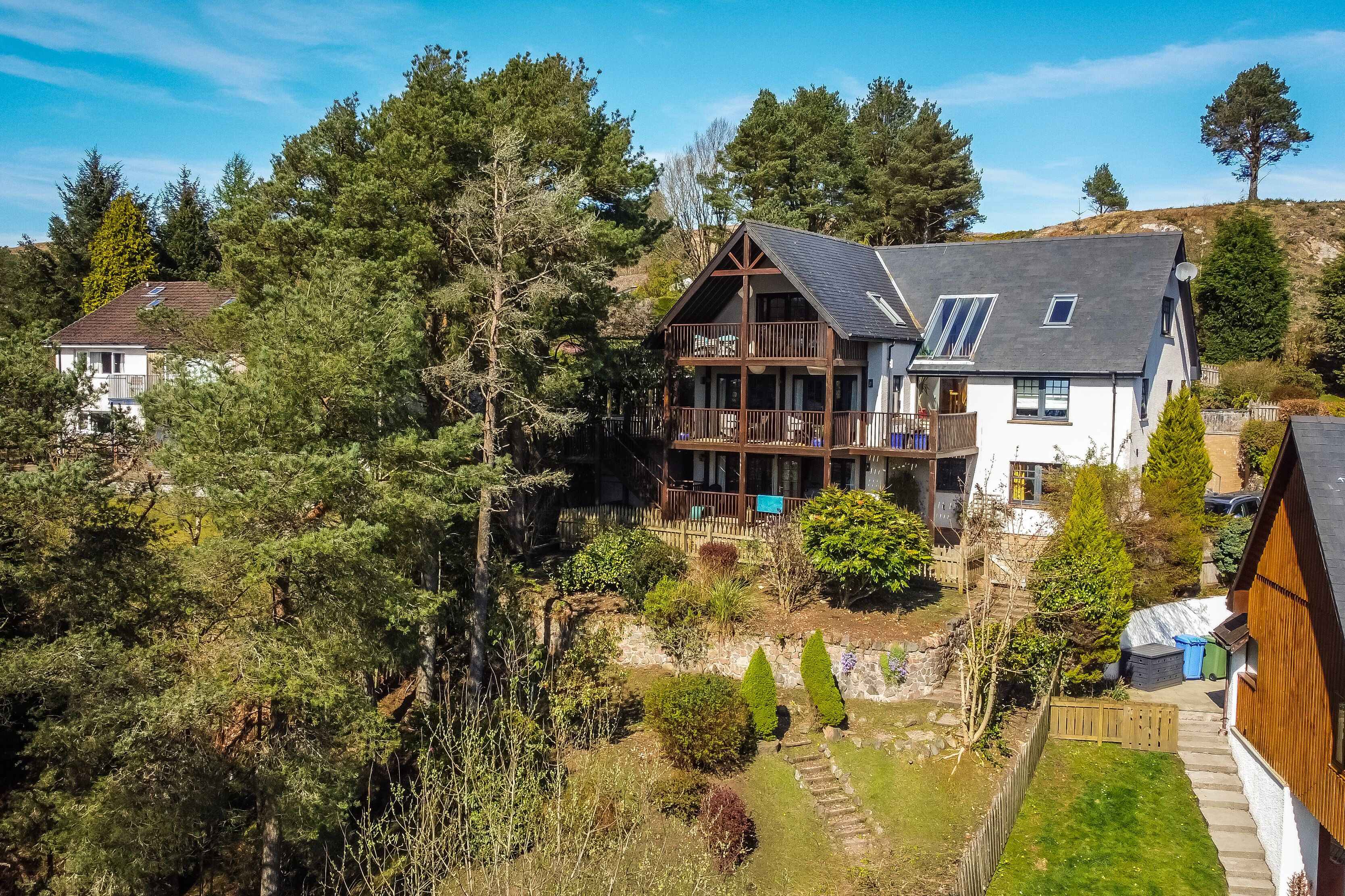 Une grande maison dotée d’un balcon, entourée d’arbres et d’un jardin.