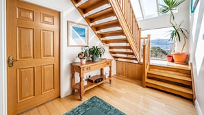 A wooden staircase with a view of the outdoors, a wooden door, a console table with plants, and a green rug. - Treetops B&B (Fort William)