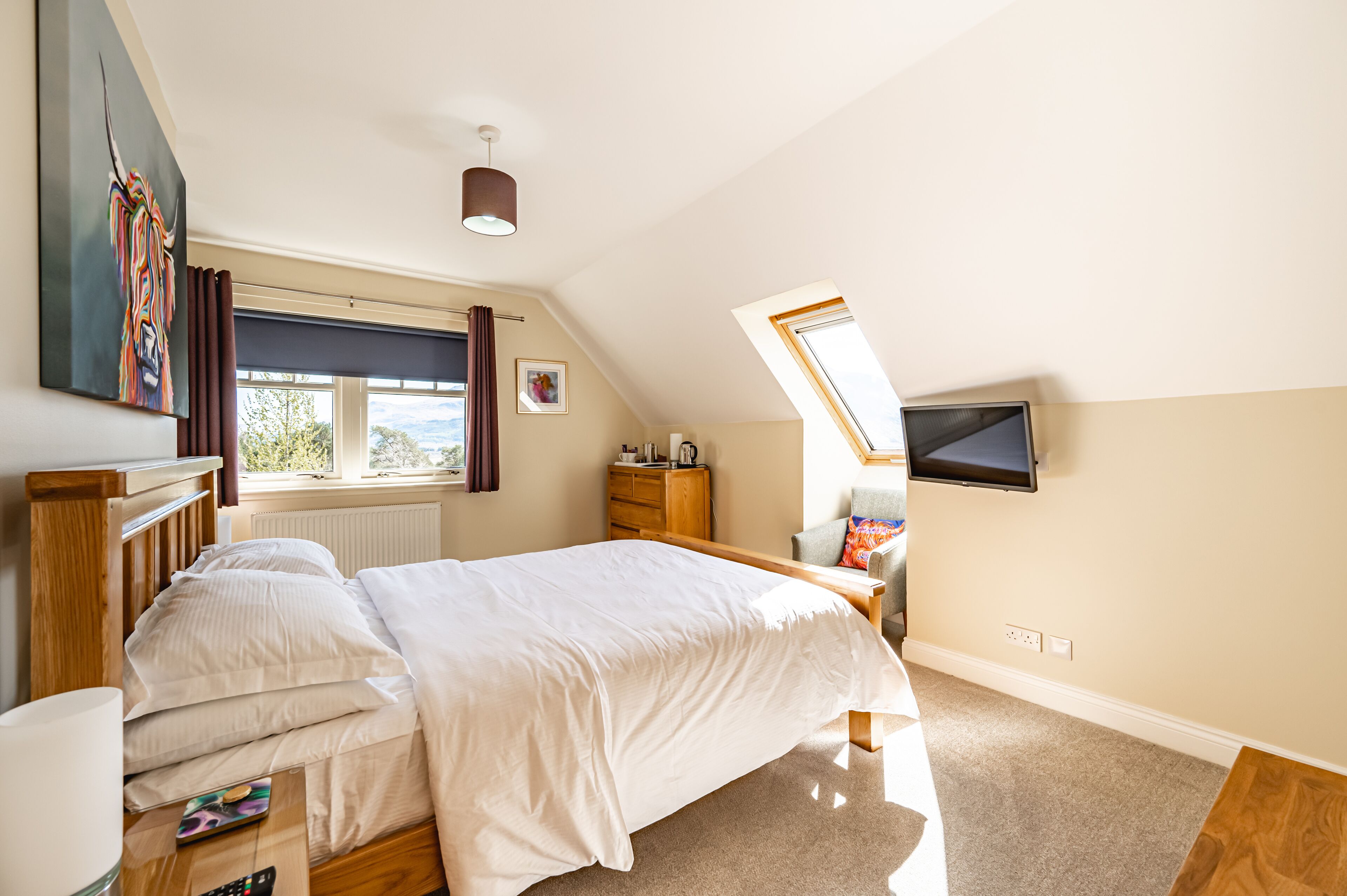 Un dormitorio con cama, televisión en la pared, ventana con cortinas y radiador.
