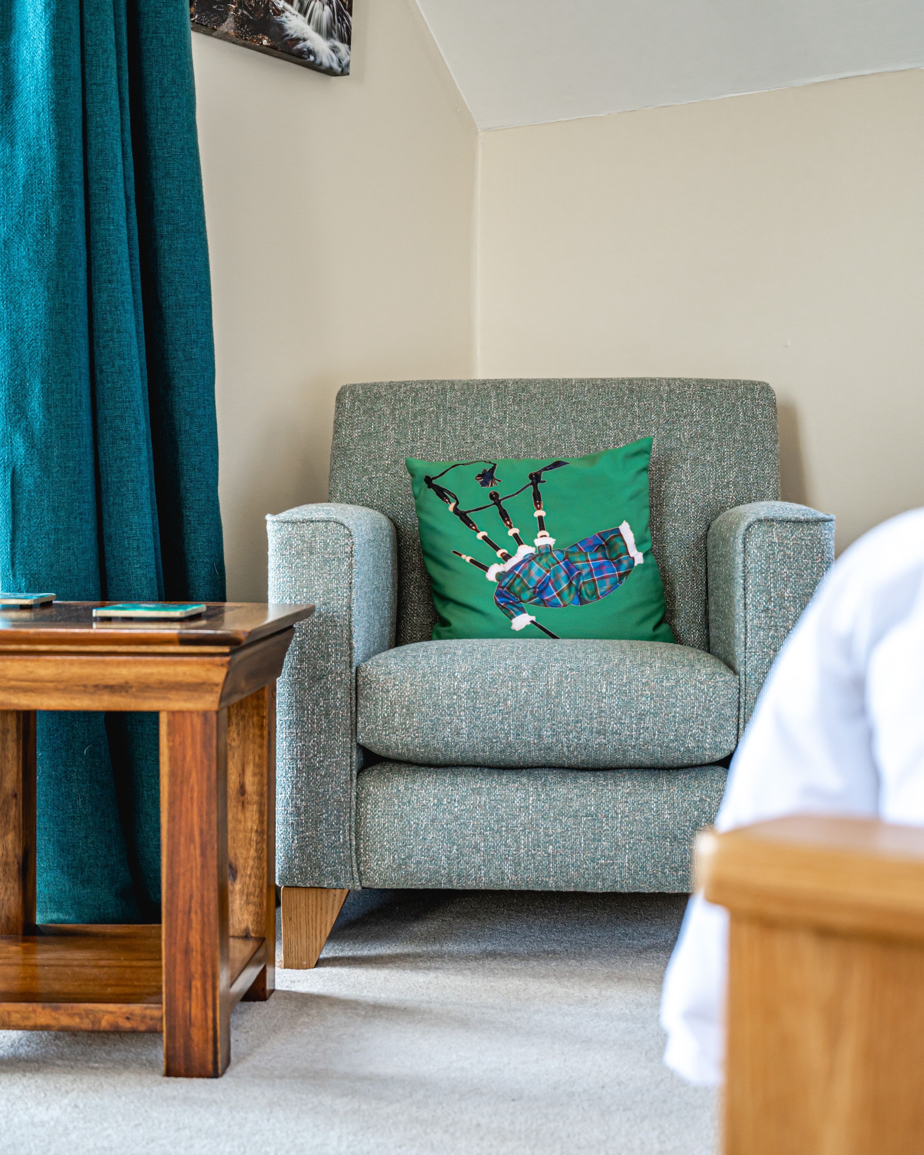 A living room with a grey armchair, a wooden coffee table, and a green pillow with a tartan design.