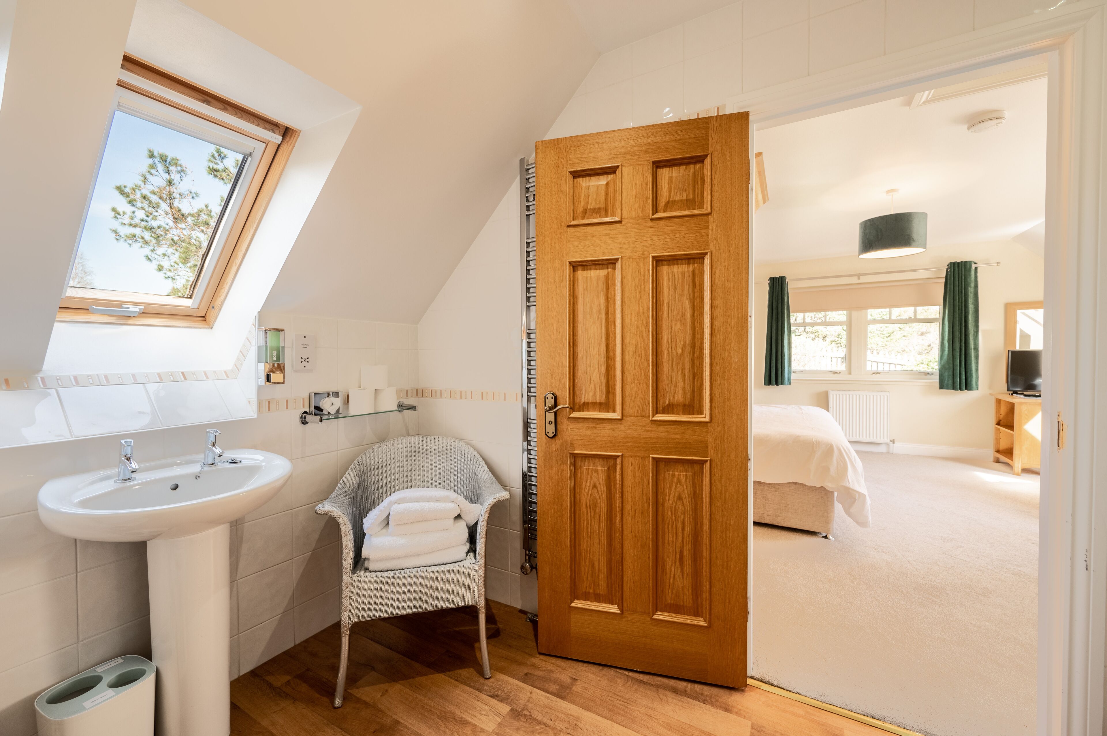 A bedroom with a wooden door, a window, a bed, and a view of the outside.
