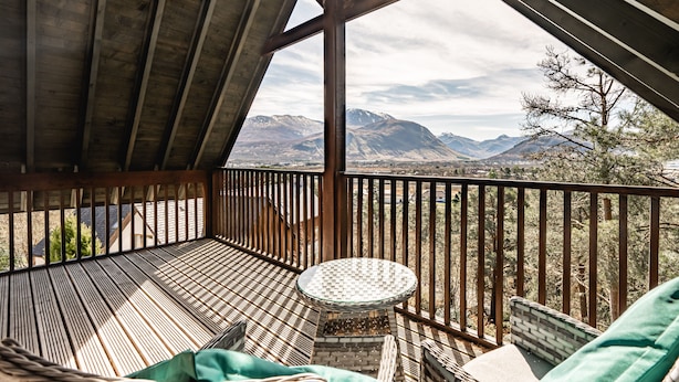 A wooden deck with a round table and seating, overlooking a mountainous landscape. - Treetops B&B (Fort William)