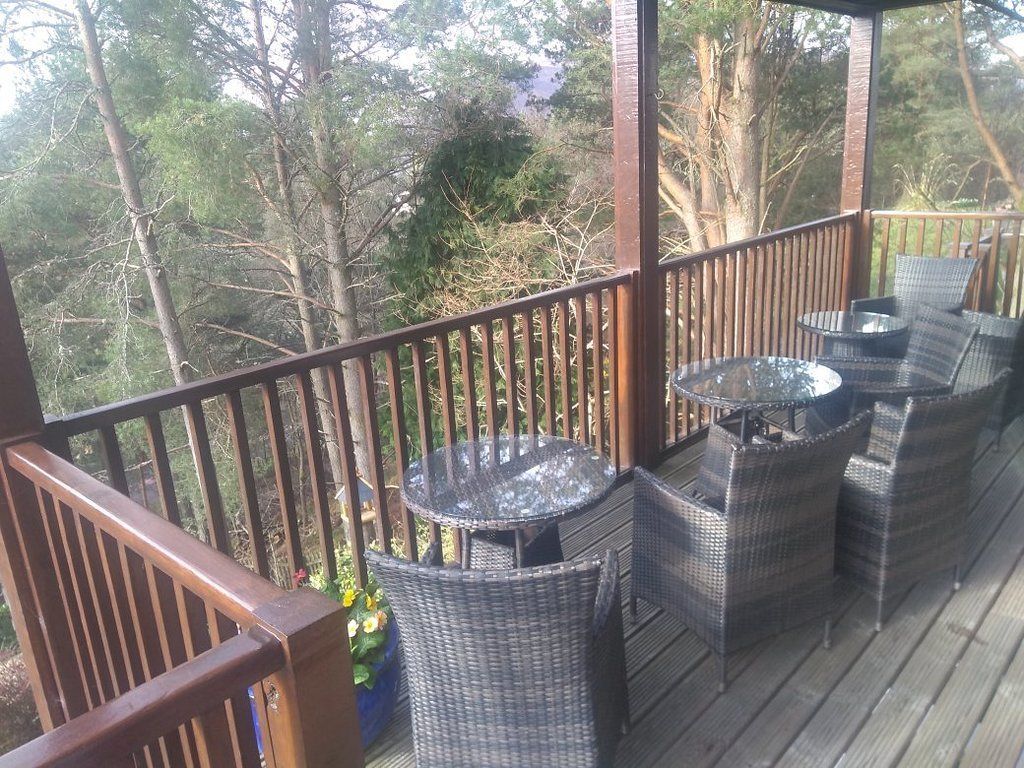 A covered outdoor deck with wicker furniture and a glass table.