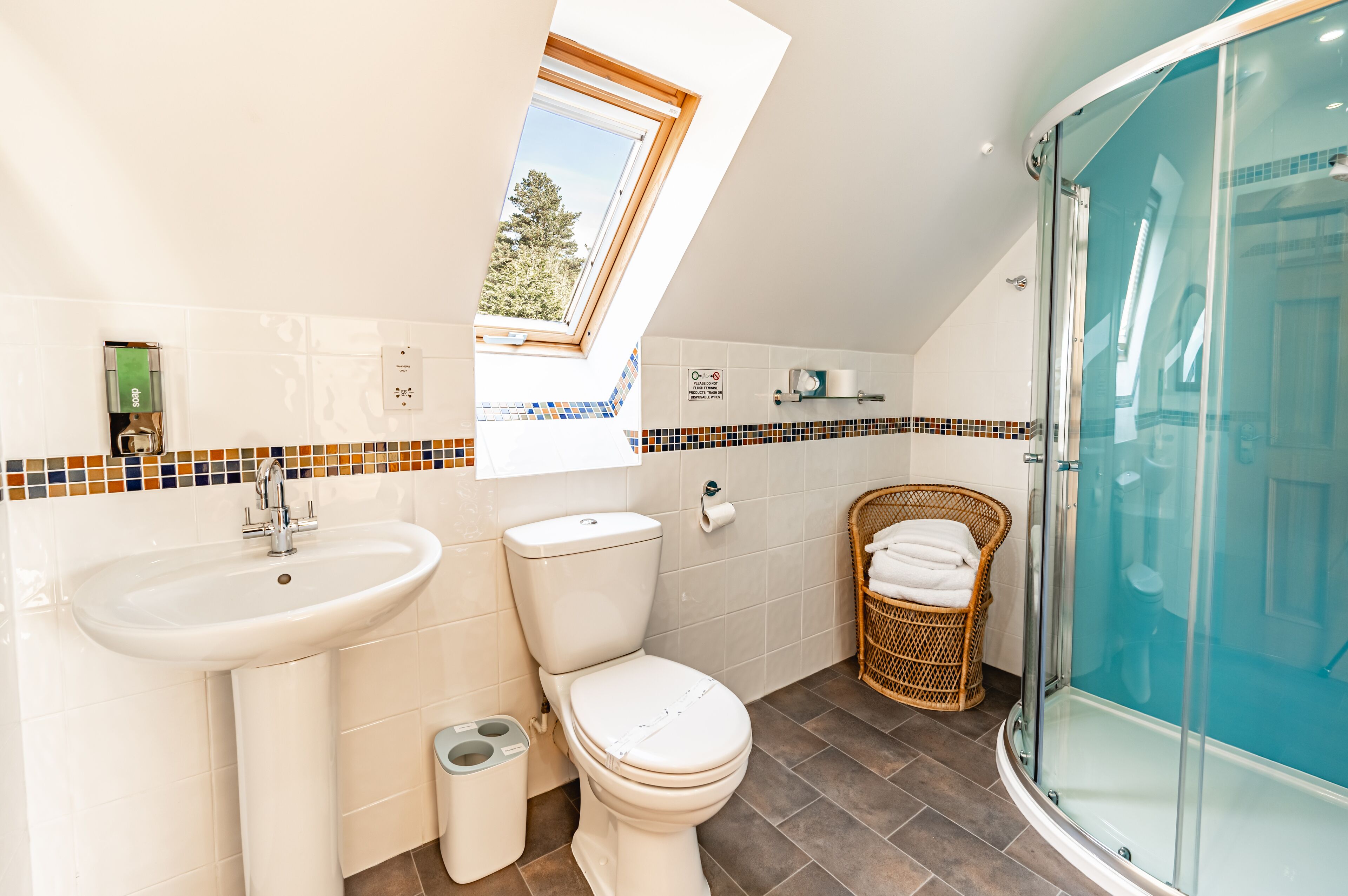 A modern bathroom with a skylight, a glass-enclosed shower, and a wicker chair.