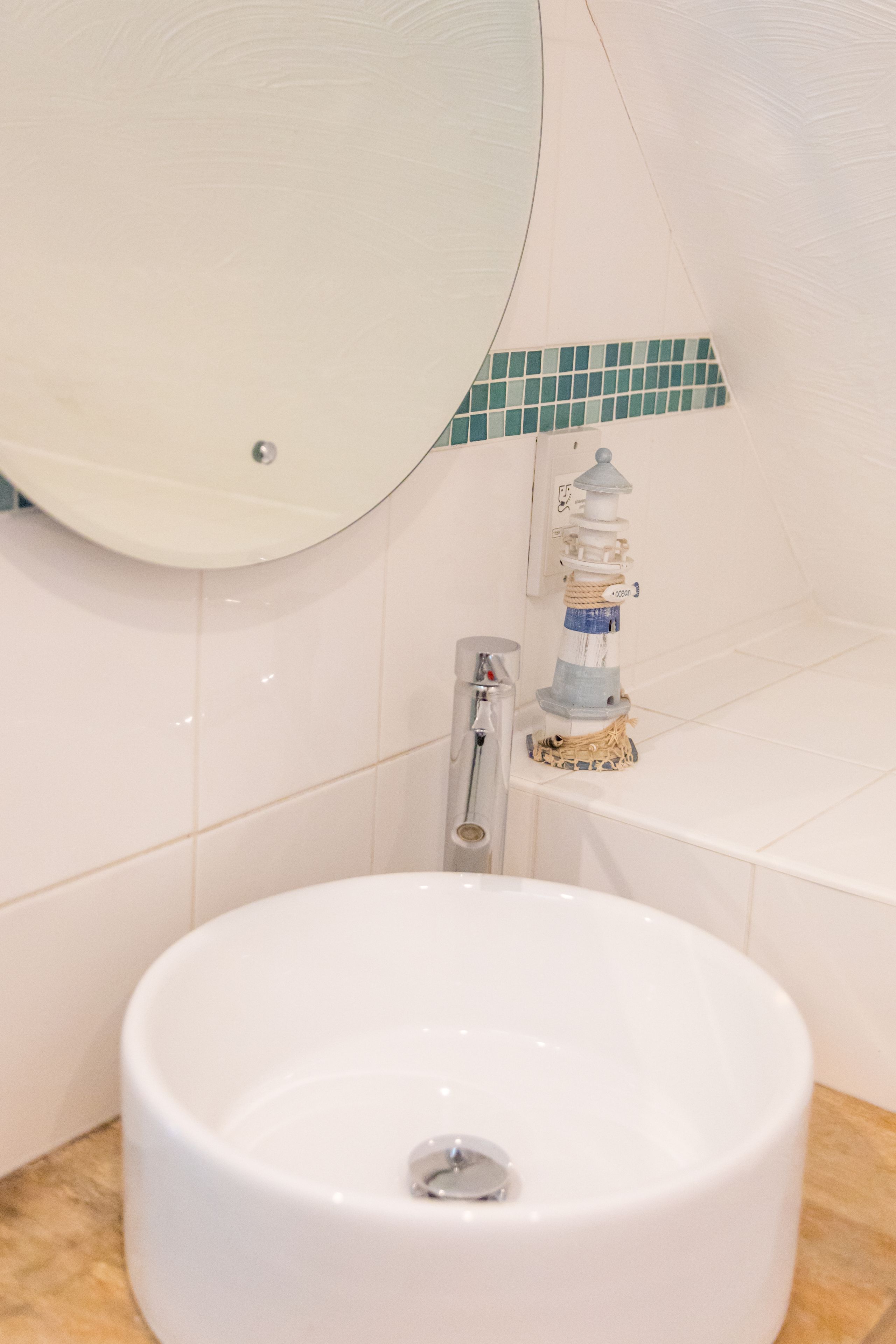 A bathroom with a round white sink, a mirror, and a small decorative lighthouse.