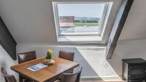 Ein Essbereich mit Tisch, Stühlen, einer Zimmerpflanze und Blick auf ein Gebäude durch eine Dachkuppel.