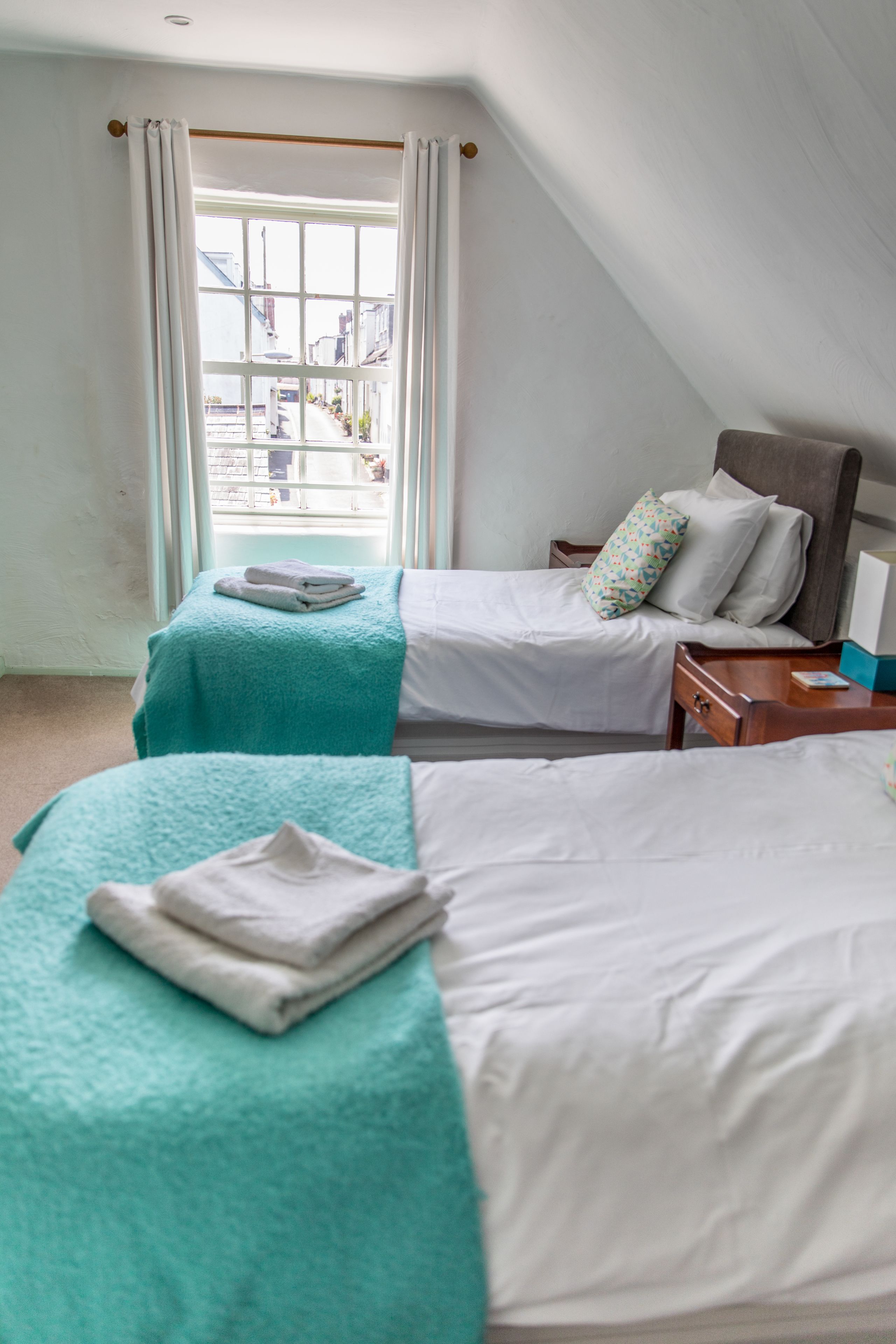 Een kamer met twee bedden, een houten hoofdbord, een nachtkastje en een raam met gordijnen.