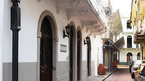 Uma rua estreita com edifícios que apresentam arcadas e um letreiro com a inscrição "P+MARALTA".