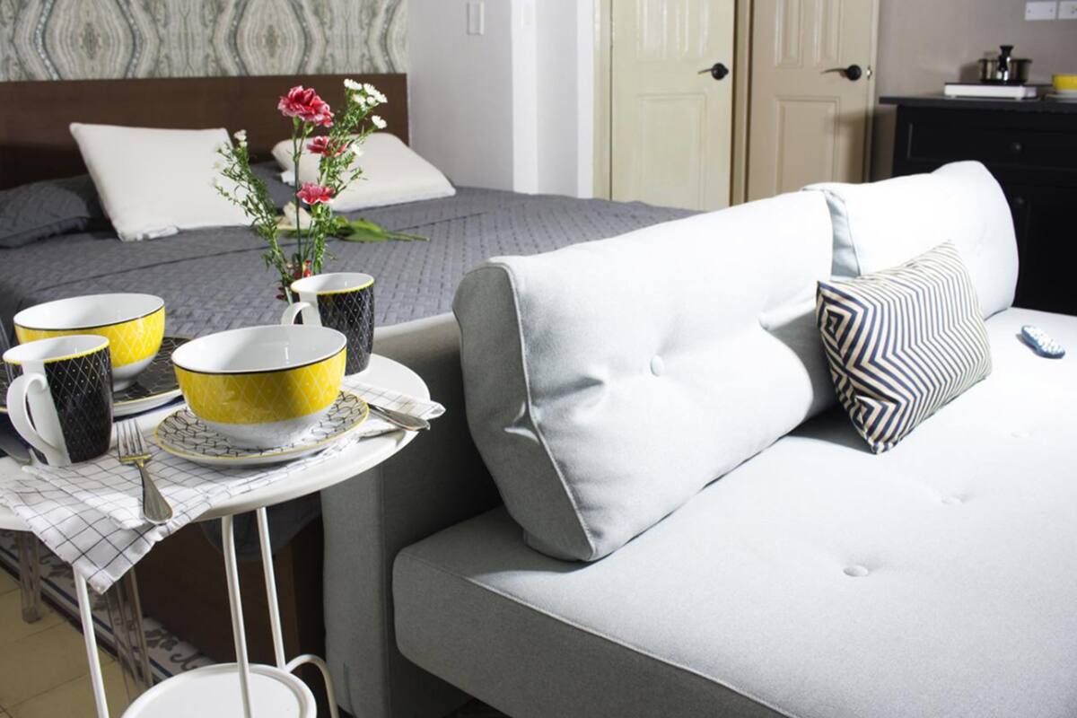 Ein ordentlich gedeckter Frühstückstisch mit gelb-schwarz gemusterten Schalen, eine Vase mit Blumen und einer Fernbedienung auf einem weißen Sofa.