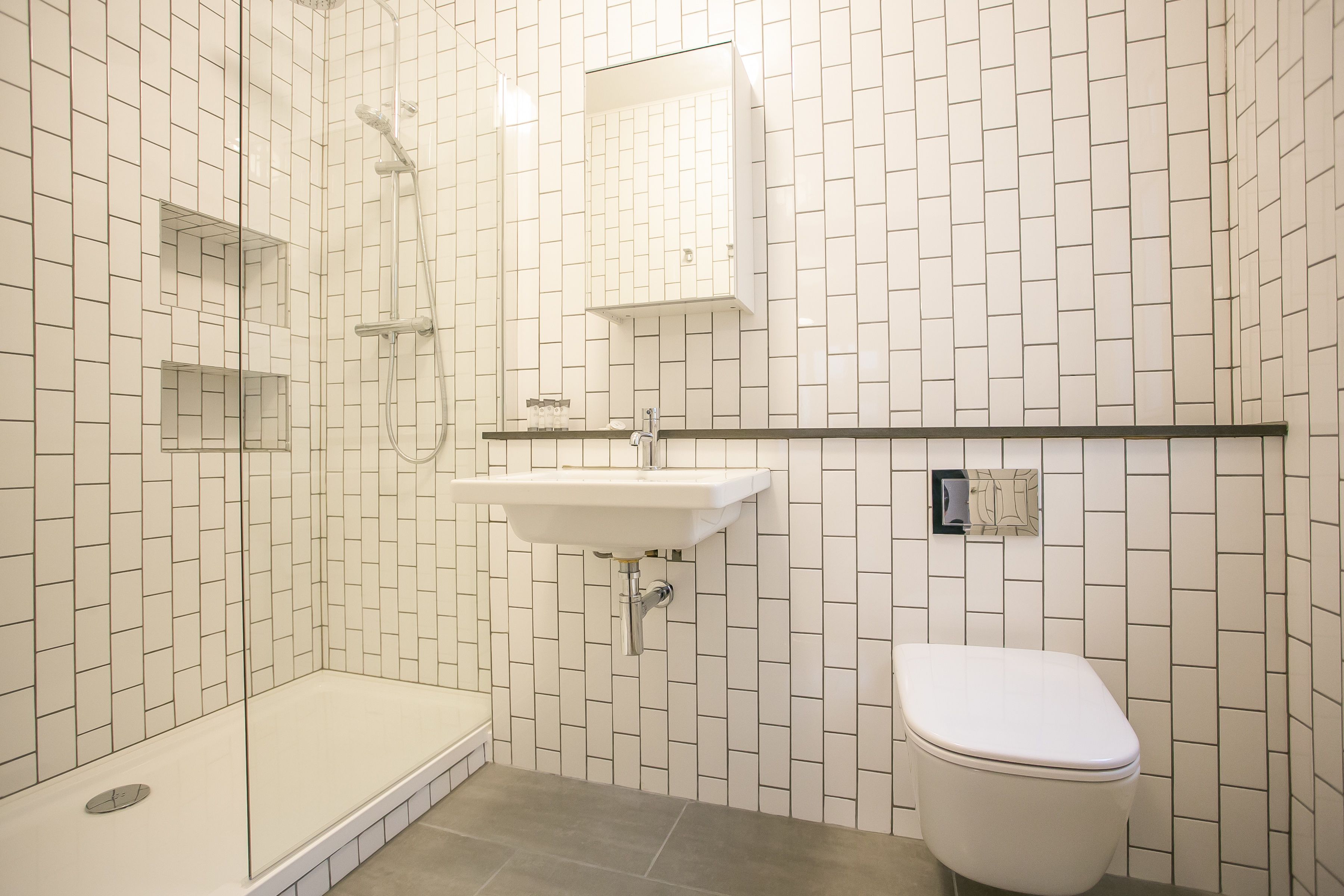 A bathroom with white tiled walls, a sink, a toilet, and a shower area.