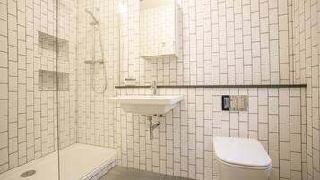 A bathroom with white tiled walls, a sink, a toilet, and a shower area.