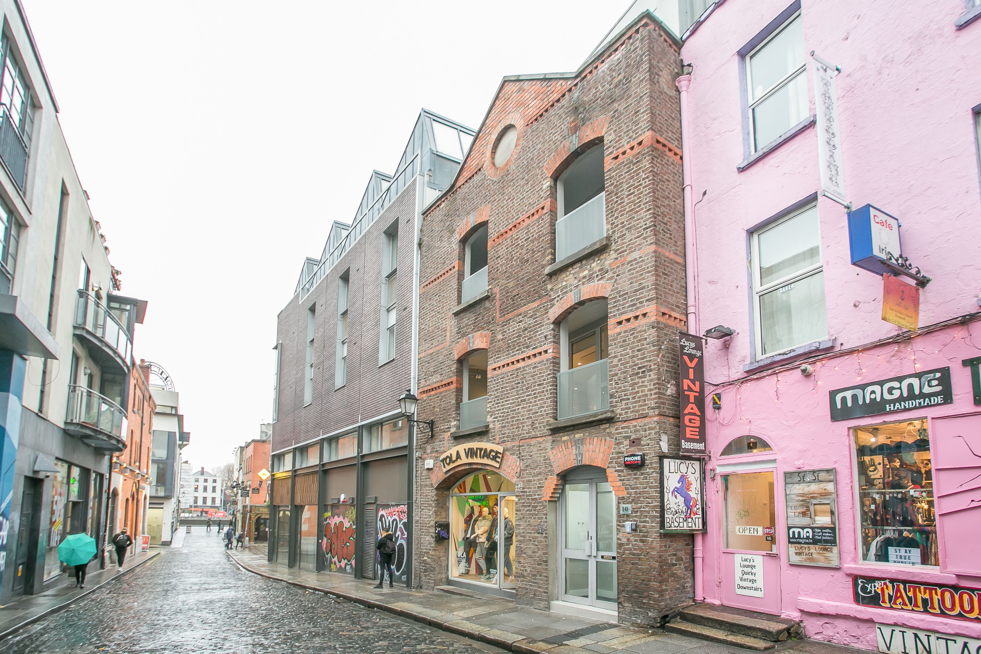 A street with vintage shops, including a pink building with a 'TATTOO' sign.