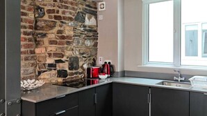 A modern kitchen with a brick accent wall, dark cabinetry, a window with a view, and a wooden floor. - Temple Bar Crowne Square Apartments (Dublin)
