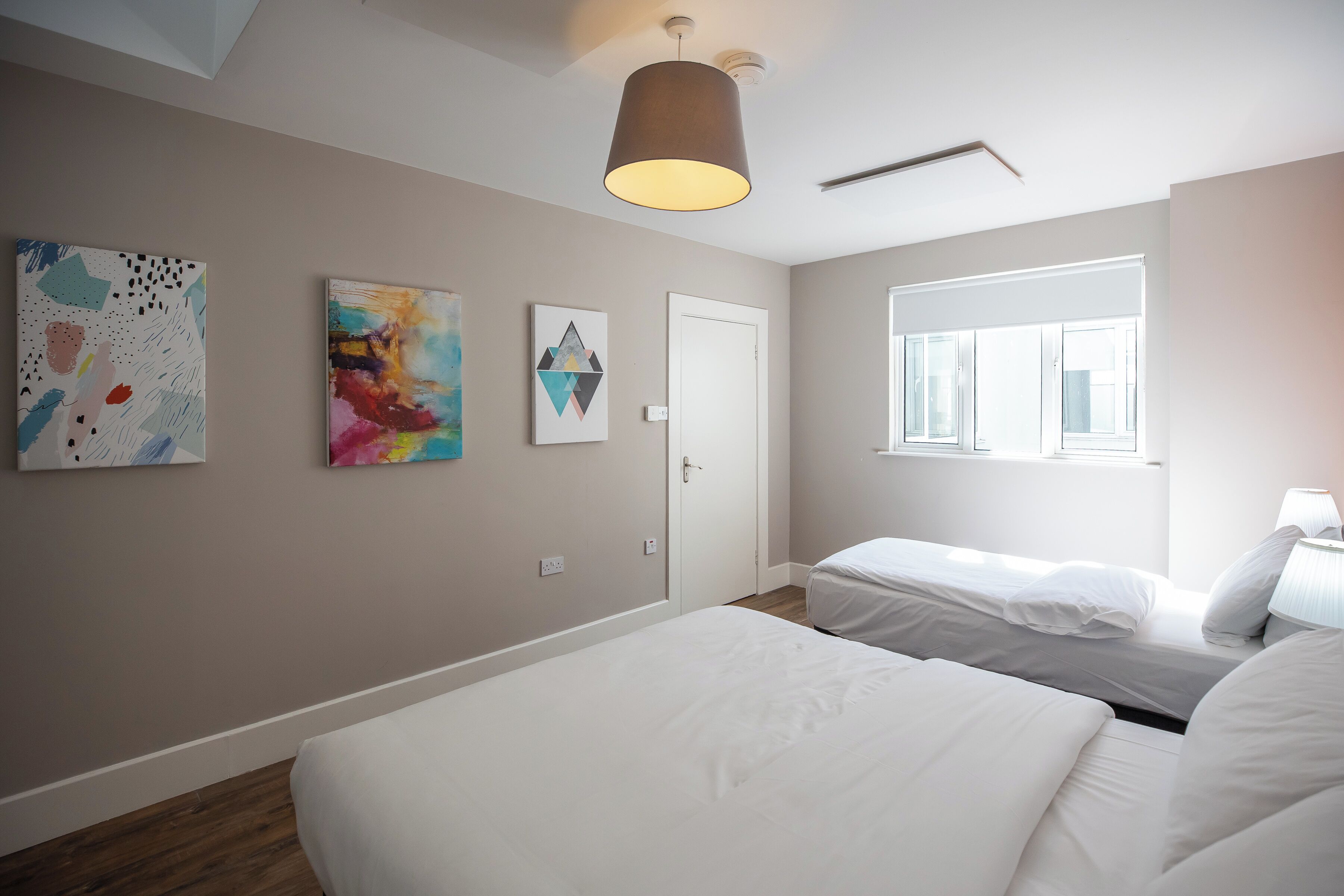 A bedroom with two beds, a window, and artwork on the walls.