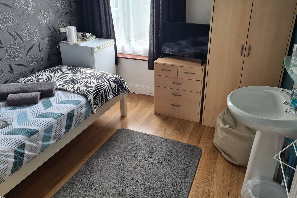 Une chambre à coucher comprenant un lit, une table de chevet, une commode et une salle de bain avec un lavabo et un miroir.