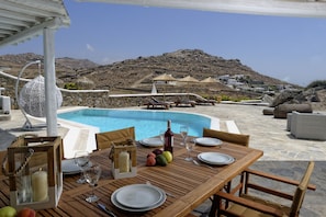 An outdoor dining area with a pool, stone walls, and a view of a mountainous landscape.