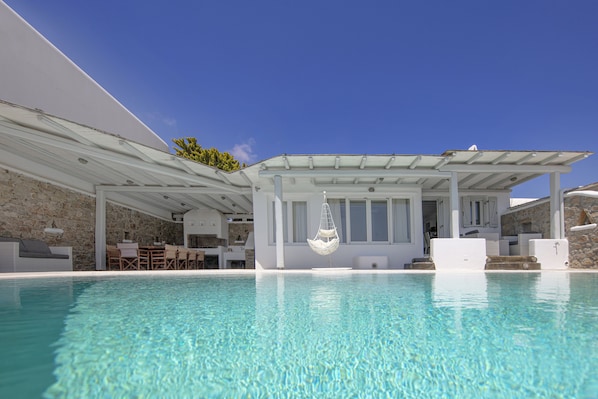 A poolside area with a covered seating area, stone walls, and a hanging chair.